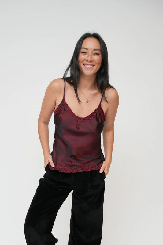 Woman wearing a burgundy satin tank top and black pants against a white background