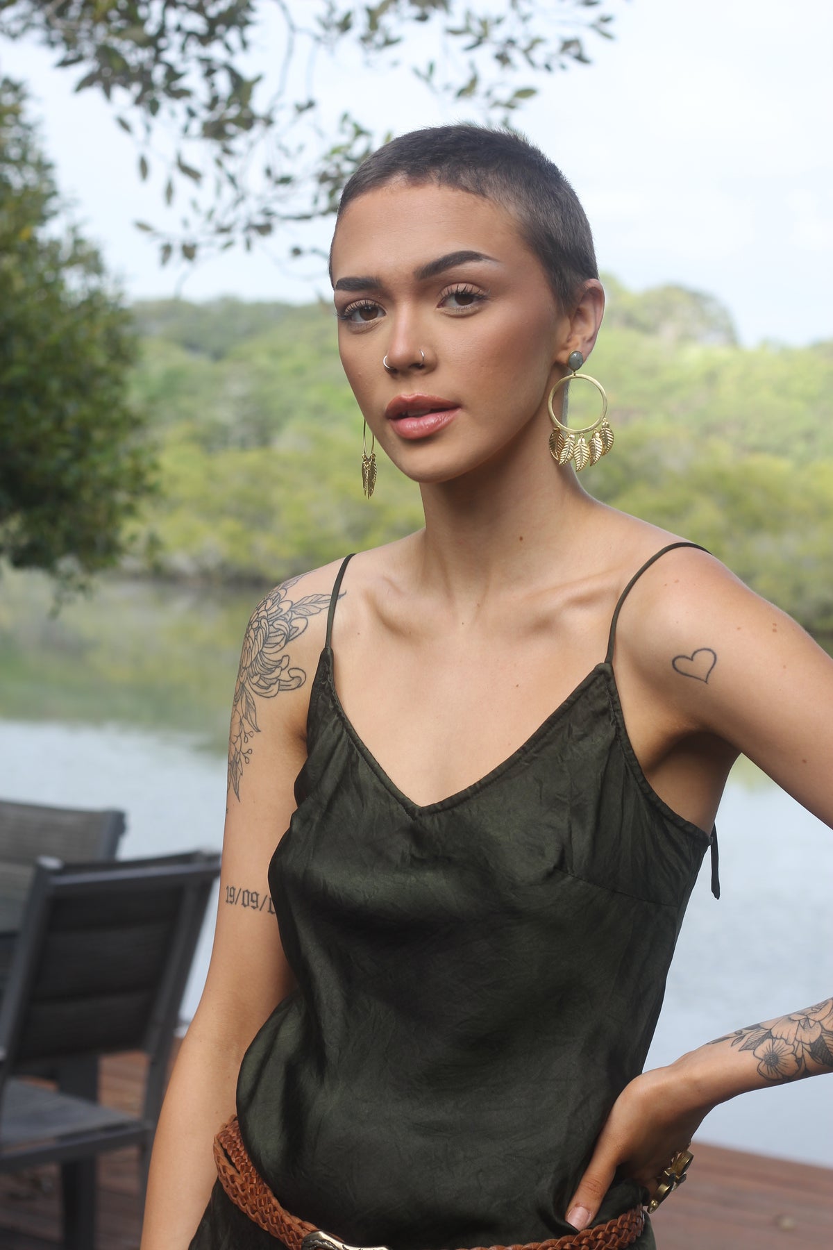 A woman wearing a black silk satin cami with adjustable tie straps, standing near a body of water.