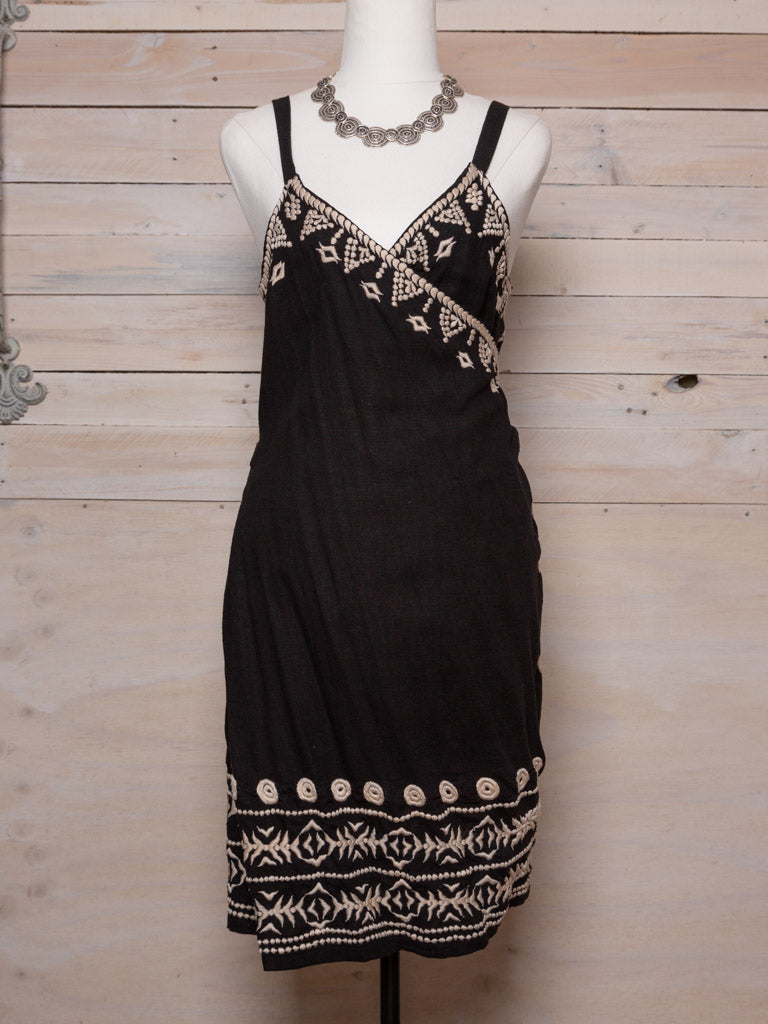 This dress features thick straps and a cross over front with ties, cream embroidered patterns at the neck and bottom hem and a natural fabric. Colour: Black with cream embroidery