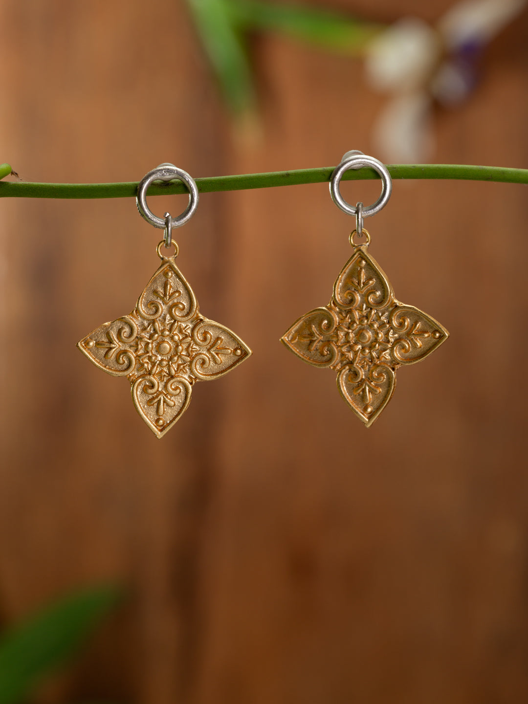 Gold cross shaped earrings with silver stud base on a backgound of blurred timber