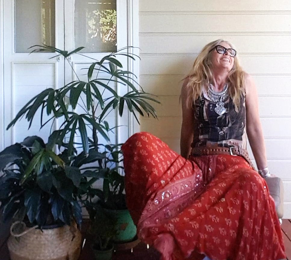 A lady stiting down with silk sari skirt in orange and band tee silver jewellery