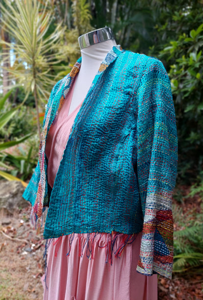 Mannequin wearing a teal knitted cardigan with colorful trim against a natural background