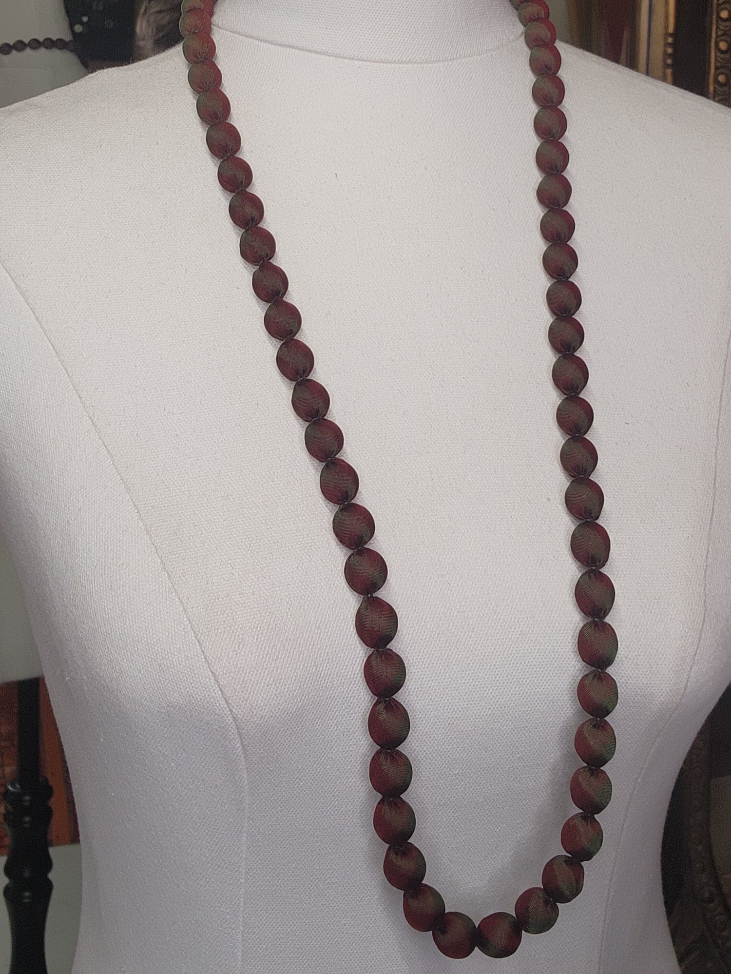 Long wooden beaded necklace on a mannequin with a plain background