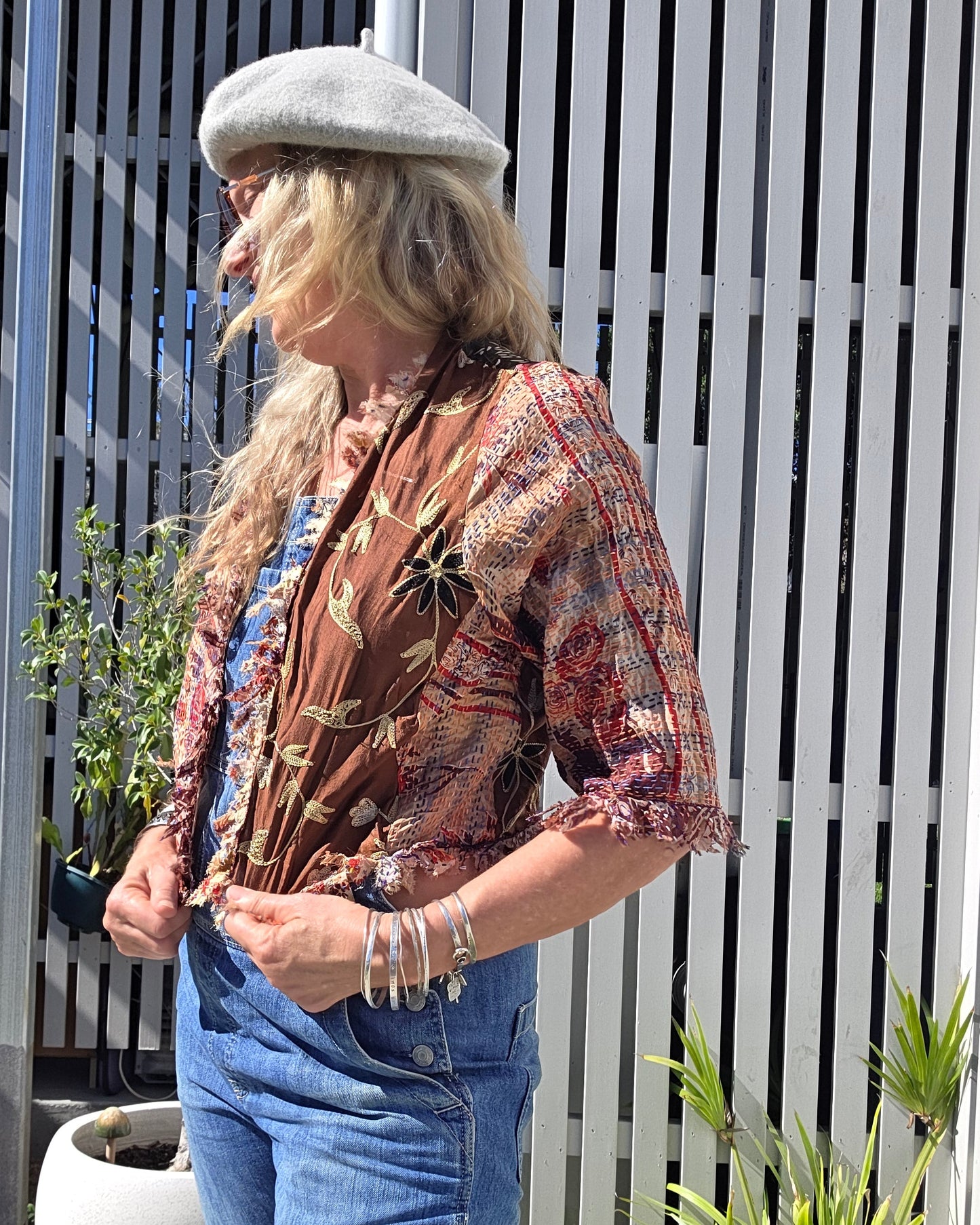 Person wearing a patterned jacket and jeans sitting on a white bench outdoors.