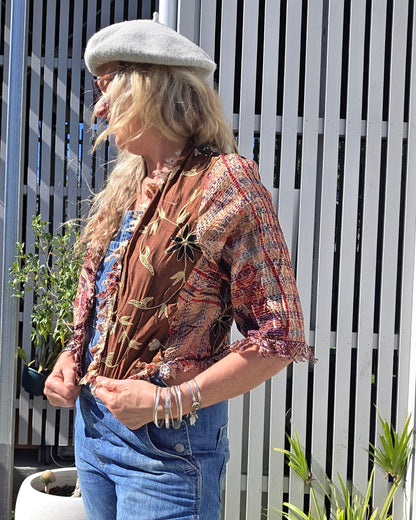 Person wearing a patterned jacket and jeans sitting on a white bench outdoors.