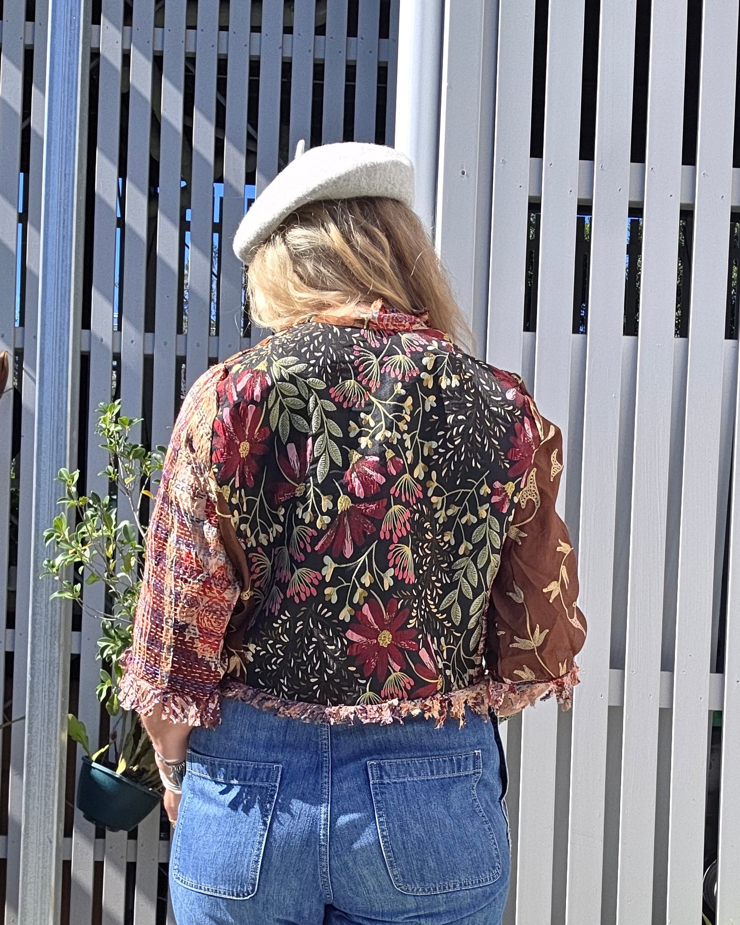 Person wearing a floral jacket and blue jeans sitting on a white bench outdoors.