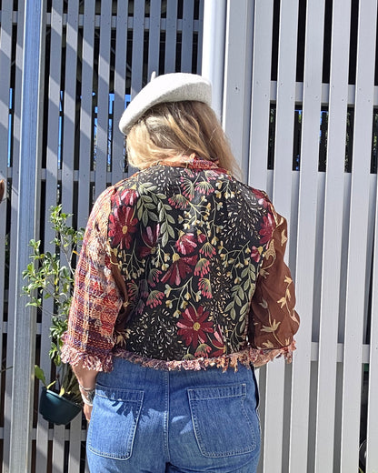 Person wearing a floral jacket and blue jeans sitting on a white bench outdoors.