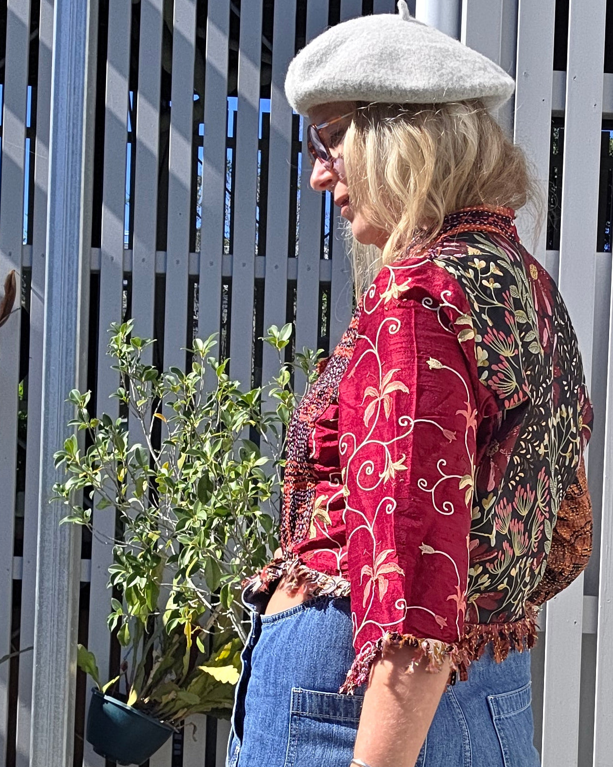 Person wearing a red patterned jacket, blue jeans, and a grey beret
