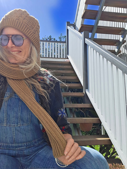 Person wearing a knit hat and sunglasses on a deck with a clear blue sky.