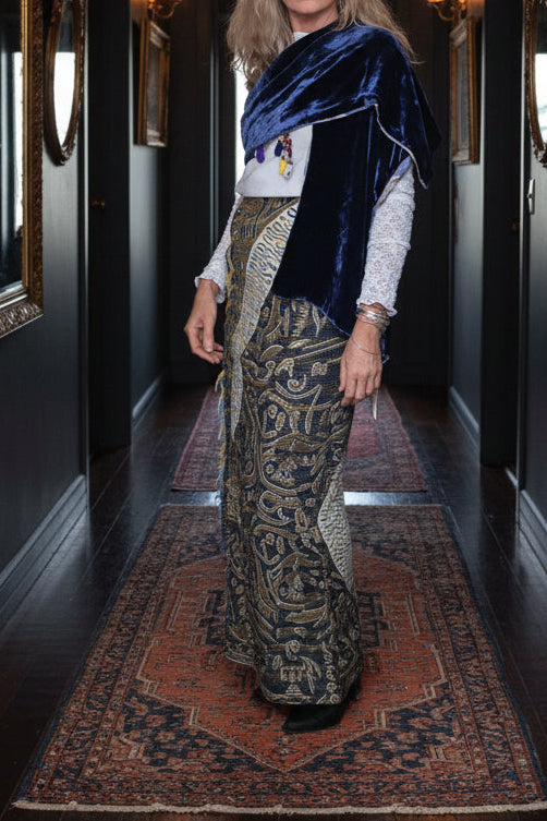 Person wearing a blue velvet shawl over a patterned garment with a mirror and room decor in the background.