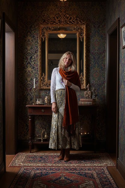 Person wearing a white lace garment sitting on a patterned chair with a wooden floor.