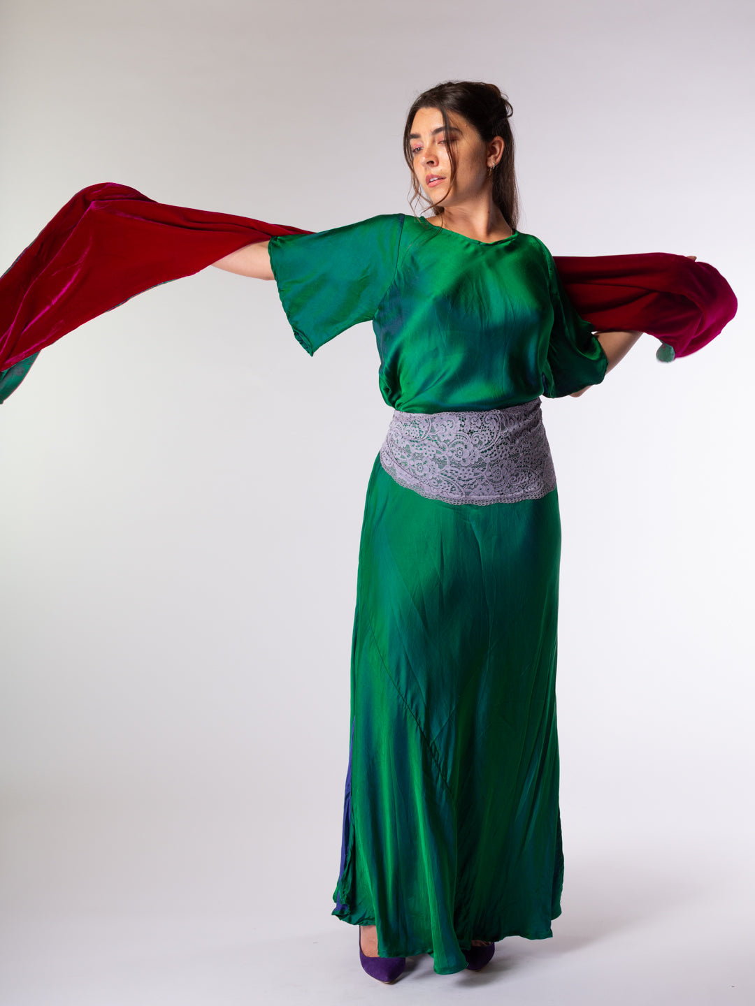 Woman in a green outfit holding a red velvet scarf against a white background