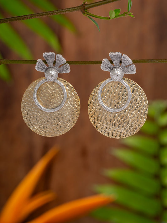 Pair of gold and silver earrings hanging on a branch with a blurred natural background