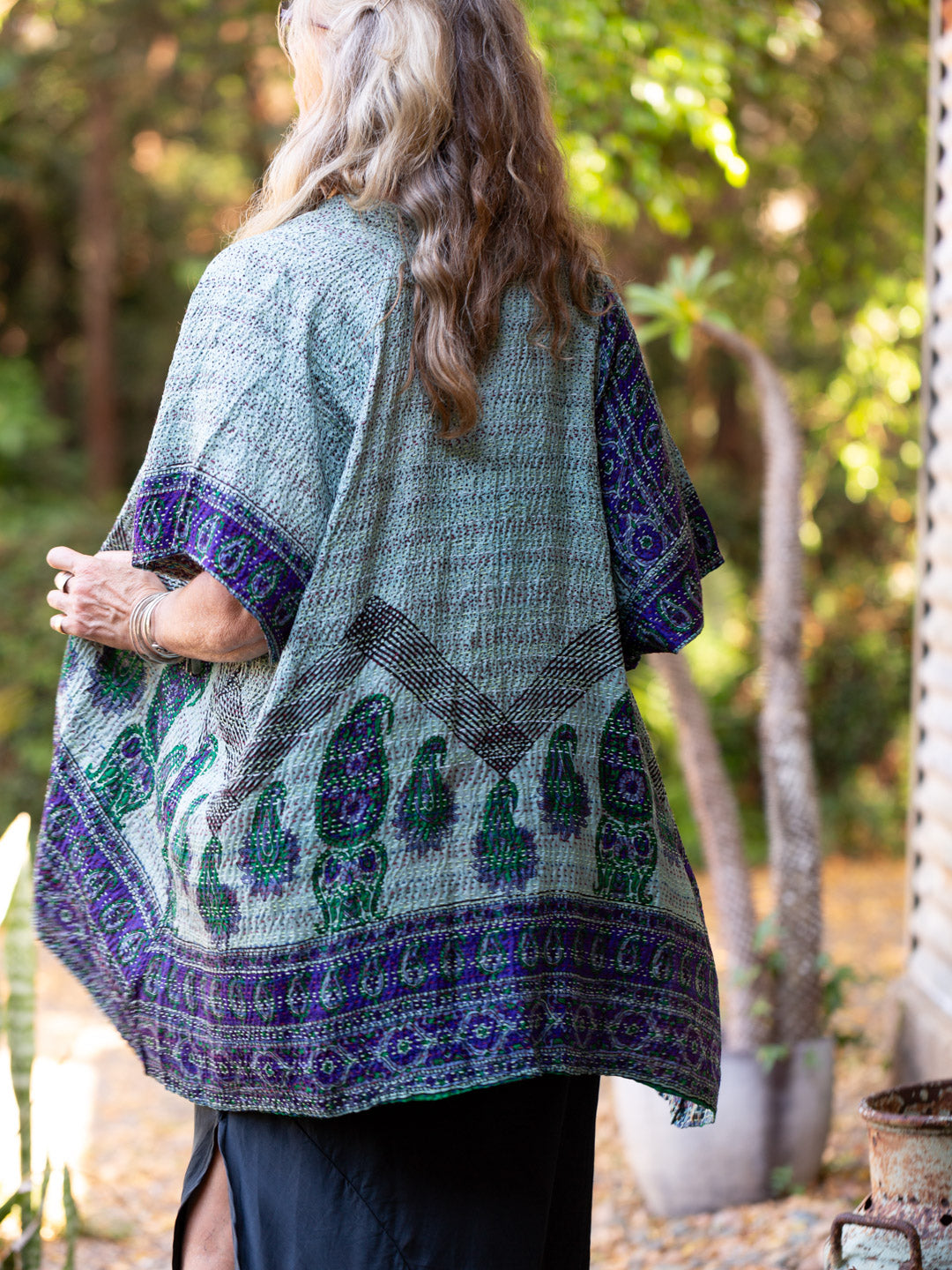 Person wearing a patterned green and purple shawl outdoors with trees in the background