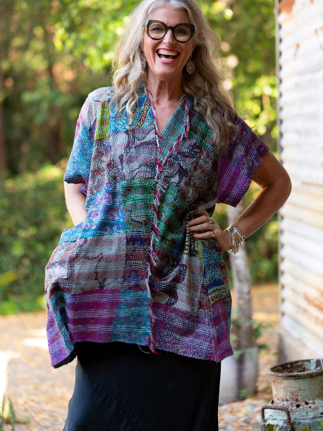 Woman wearing a colorful patterned shirt outdoors with trees in the background