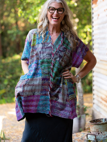 Woman wearing a colorful patterned shirt outdoors with trees in the background