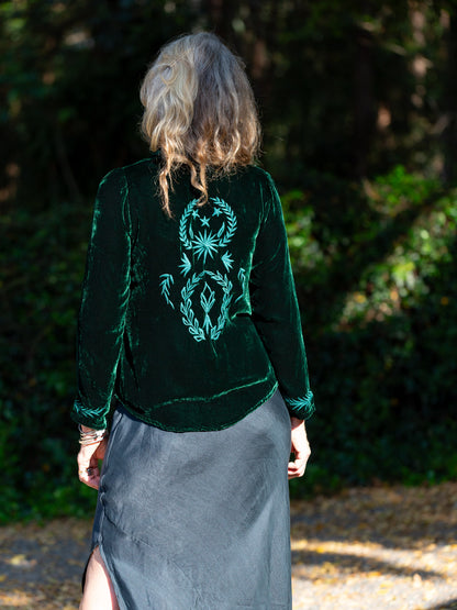Person wearing a dark green velvet jacket with a teal embroidered design, standing outdoors.