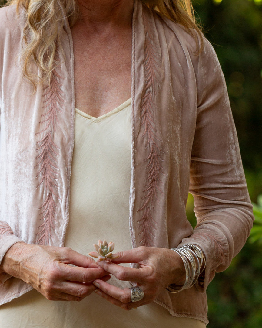Person wearing a dusty pink velvet jacket with a blurred natural background