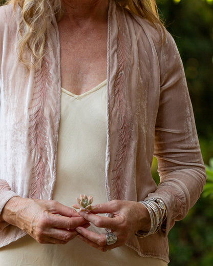 Person wearing a dusty pink velvet jacket with a blurred natural background