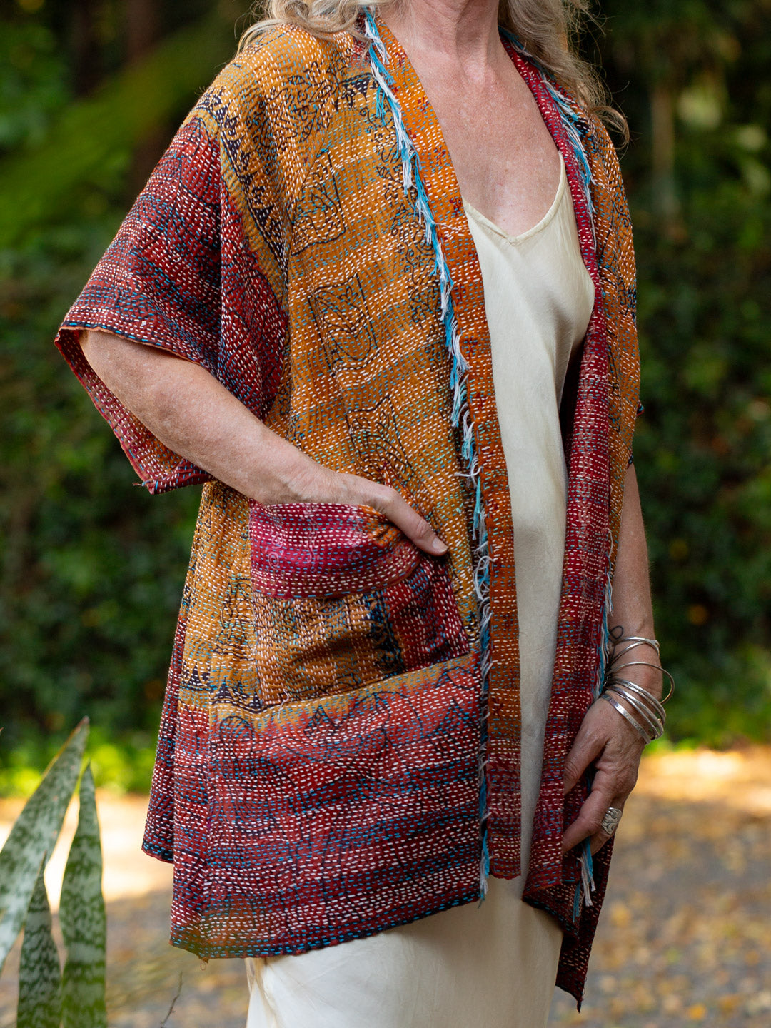 Person wearing a colorful patterned jacket outdoors with greenery in the background