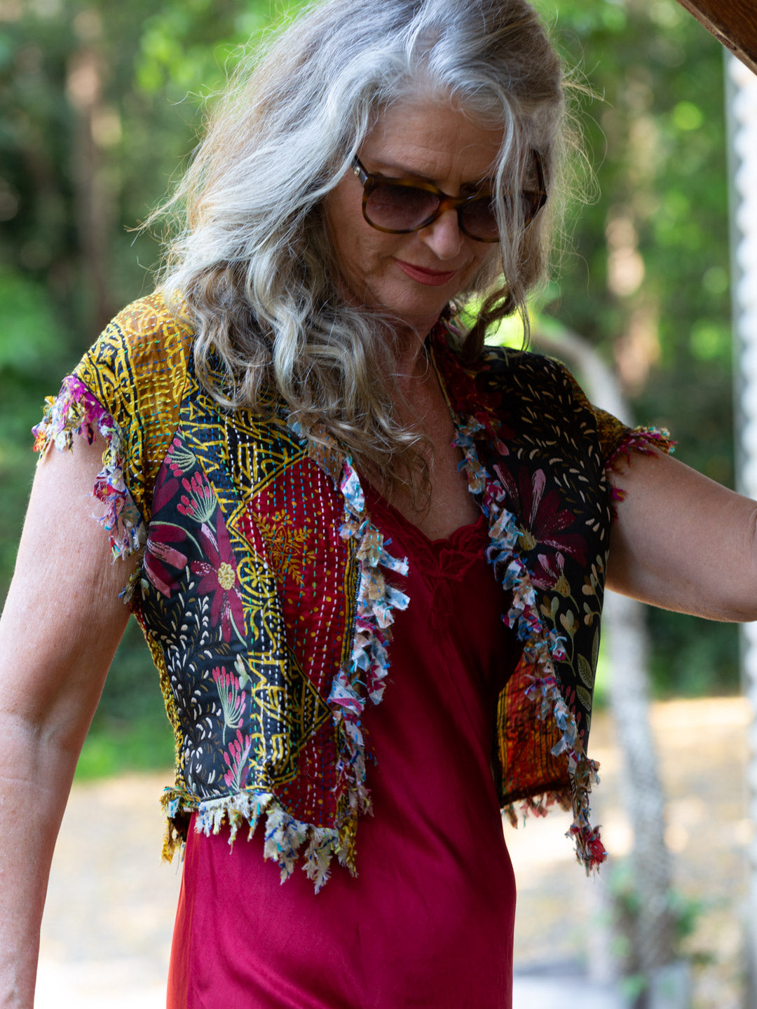 Woman wearing a colorful stitched vest over a pink dress with a blurred natural background