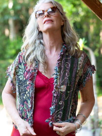 Woman wearing a colorful patterned vest over a red top with sunglasses, standing outdoors.