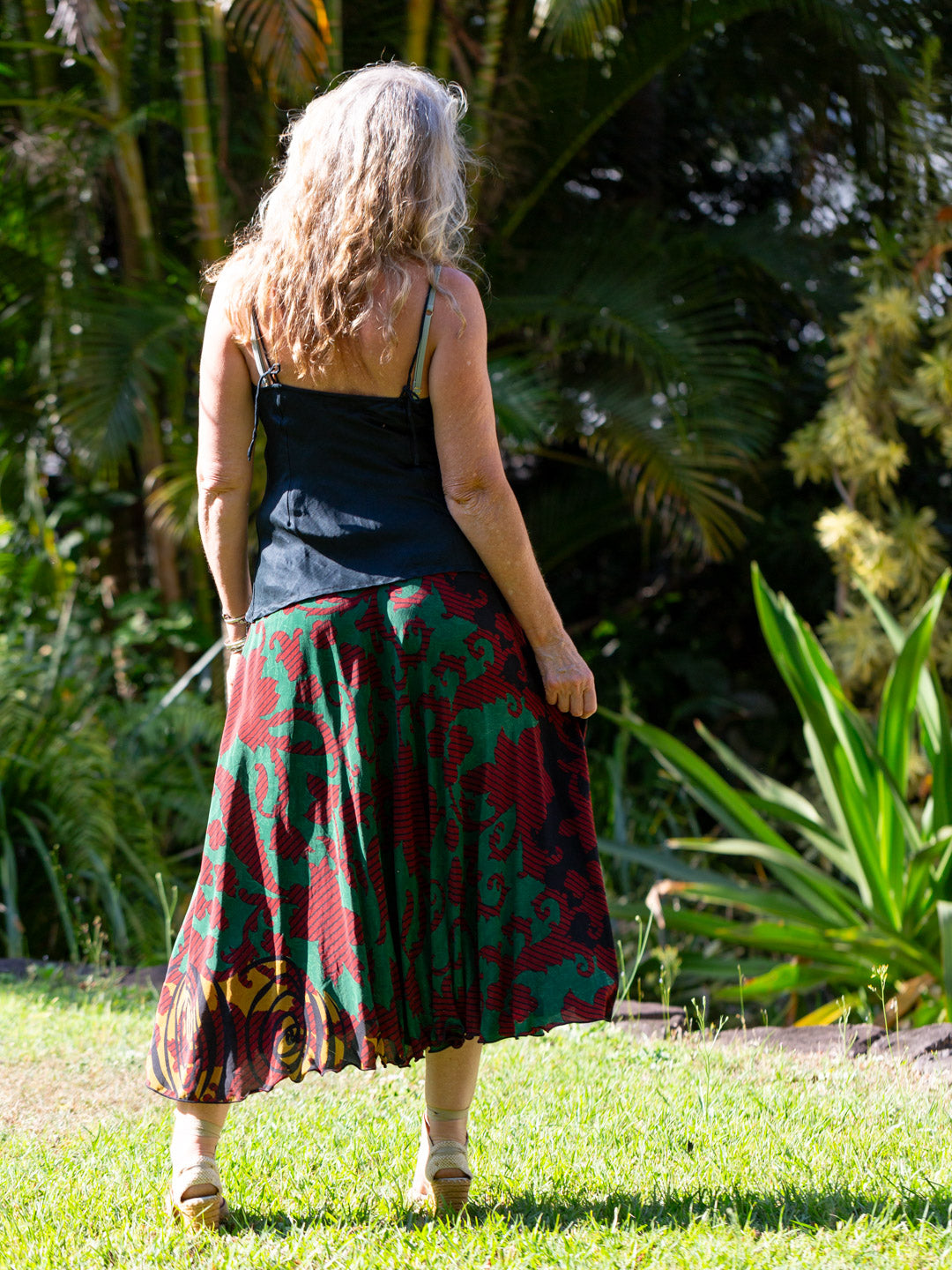 Woman wearing a black top and red patterned skirt standing in a garden.
