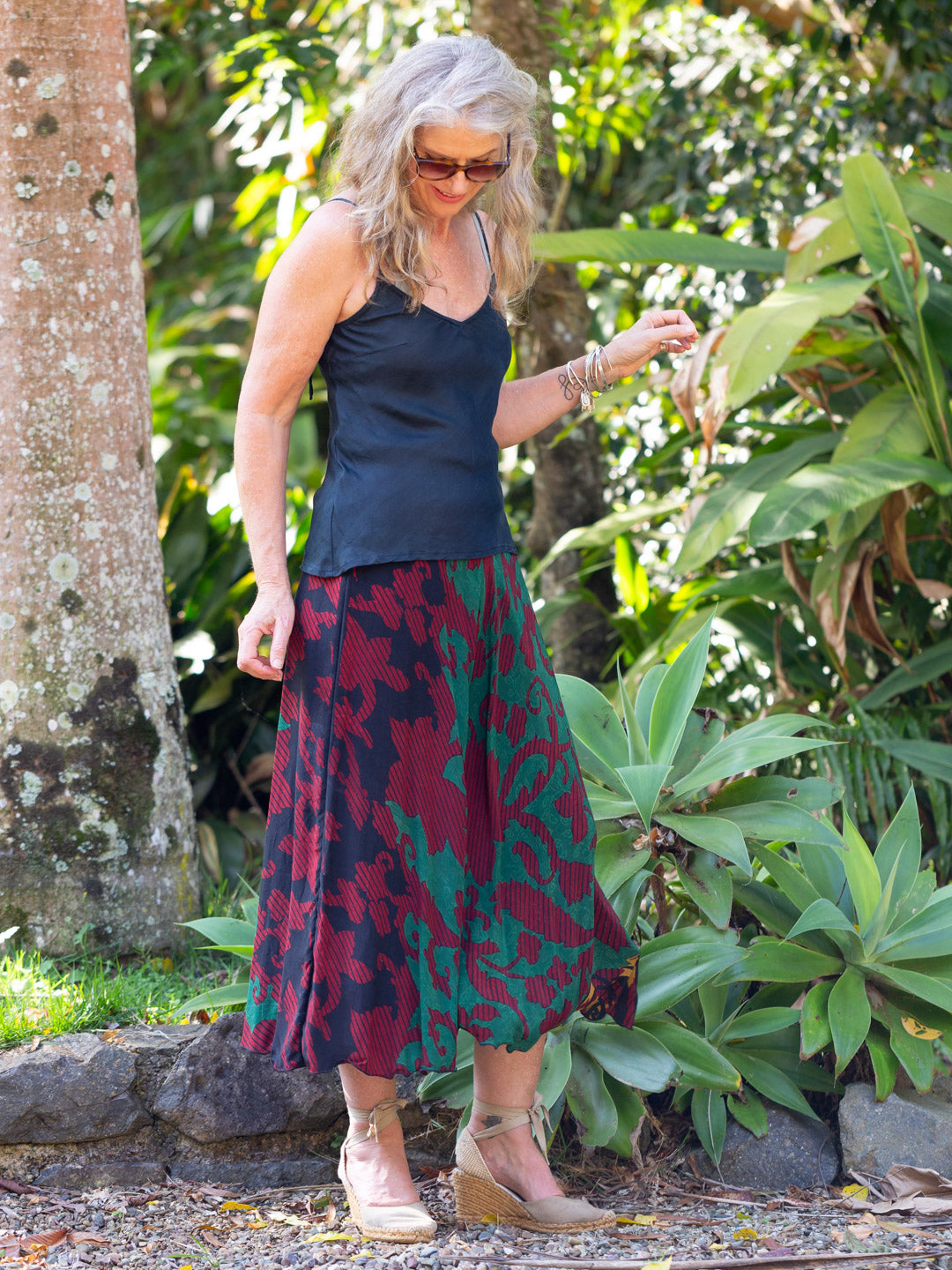 Woman in a garden wearing a navy top and patterned skirt.