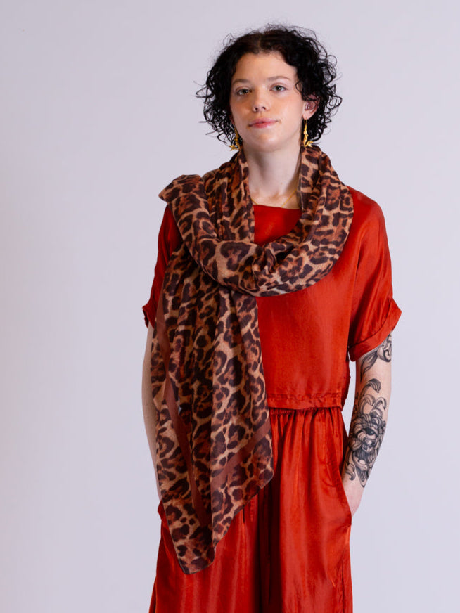 Woman wearing a rust red outfit with a leopard print scarf on a white background