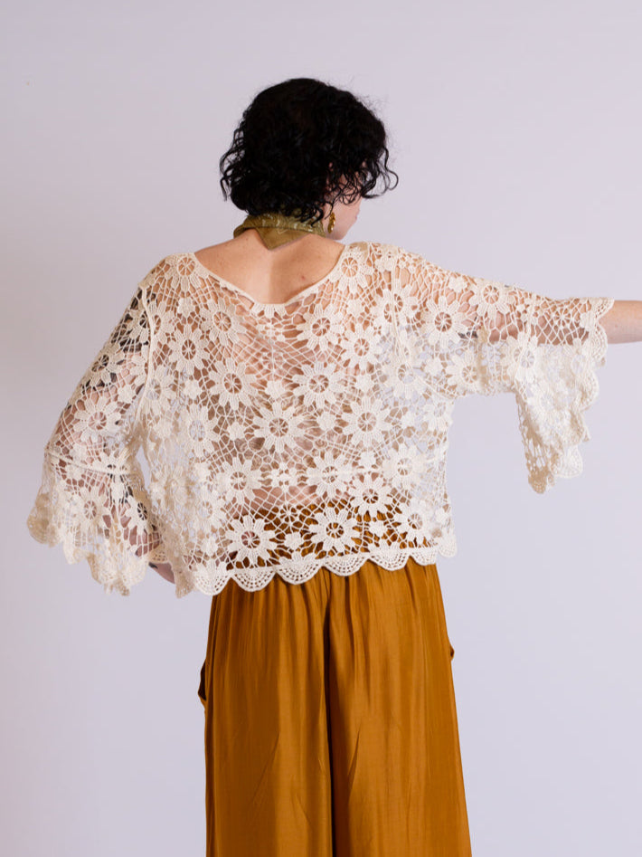 Woman wearing a floral crochet lace blouse and mustard skirt against a white background