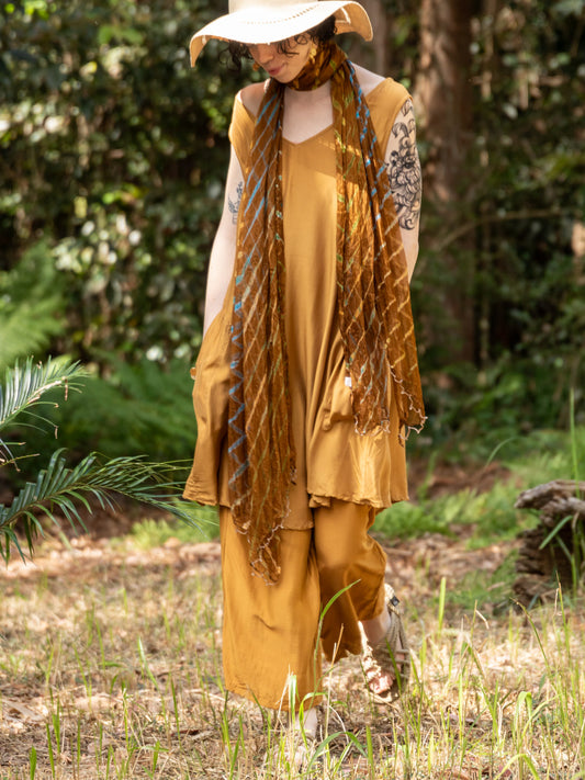 Person in mustard yellow outfit with scarf standing in a forest setting