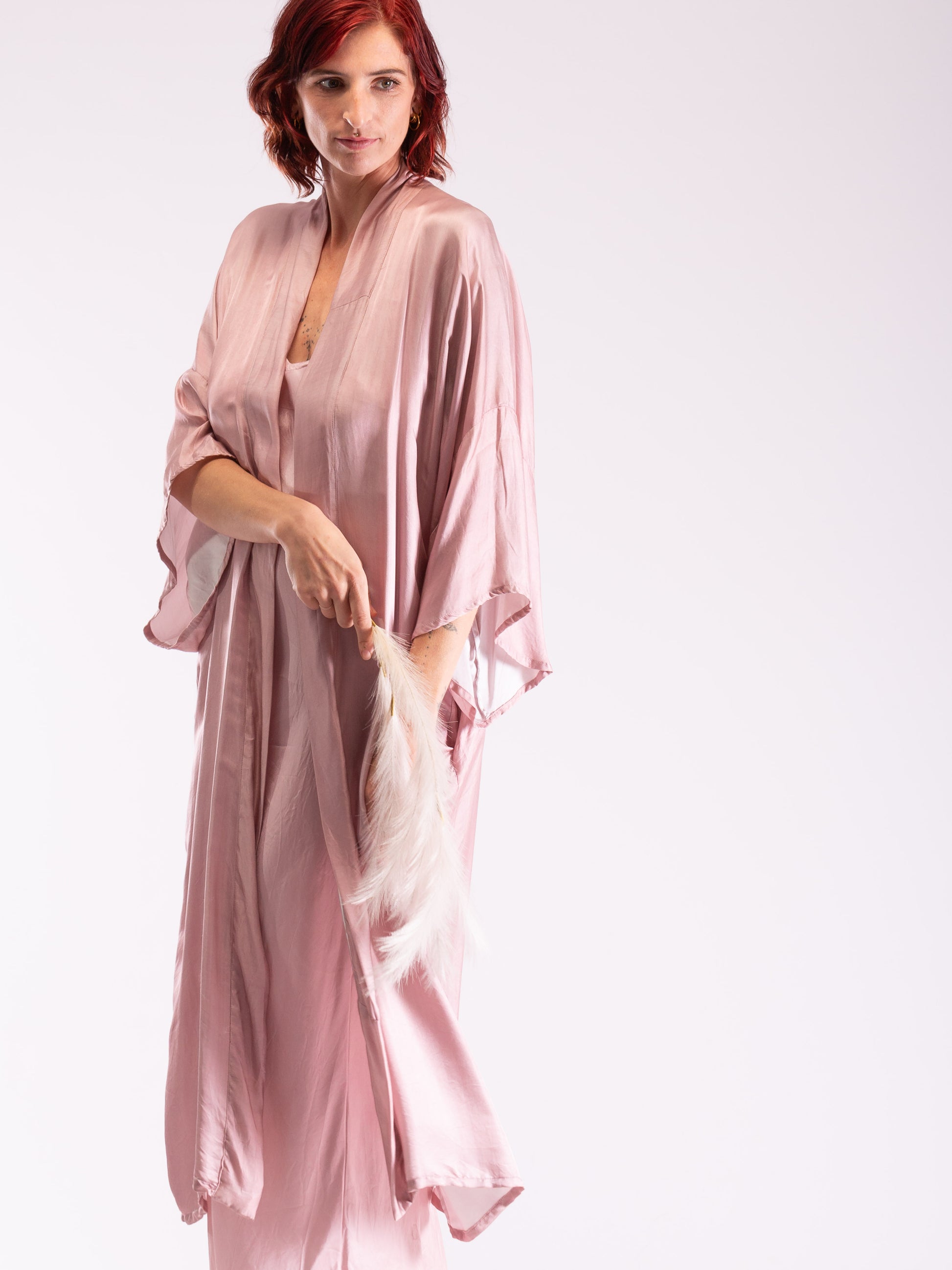 Woman wearing a pink satin robe holding a white lace garment against a white background