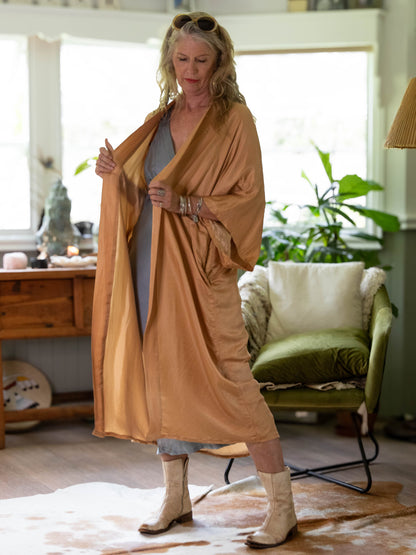 Woman in a beige robe standing in a living room with plants and furniture.