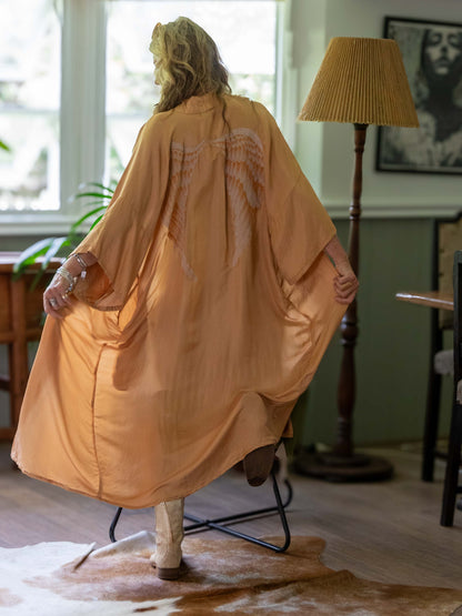 Person wearing a long, champagne kimono in a room with a lamp and window.