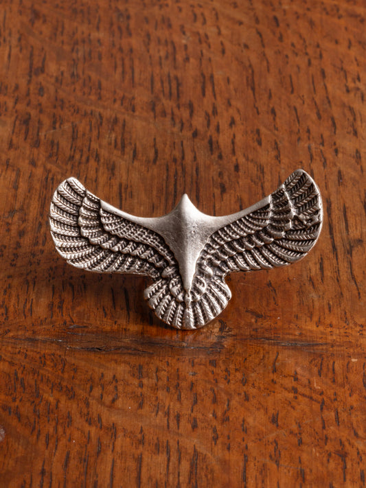 A silver-toned metal eagle ring with textured wings, displayed on a warm brown wooden surface.