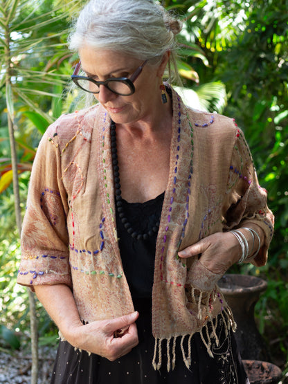 Woman wearing a beige finged jacket with colorful patterns outdoors