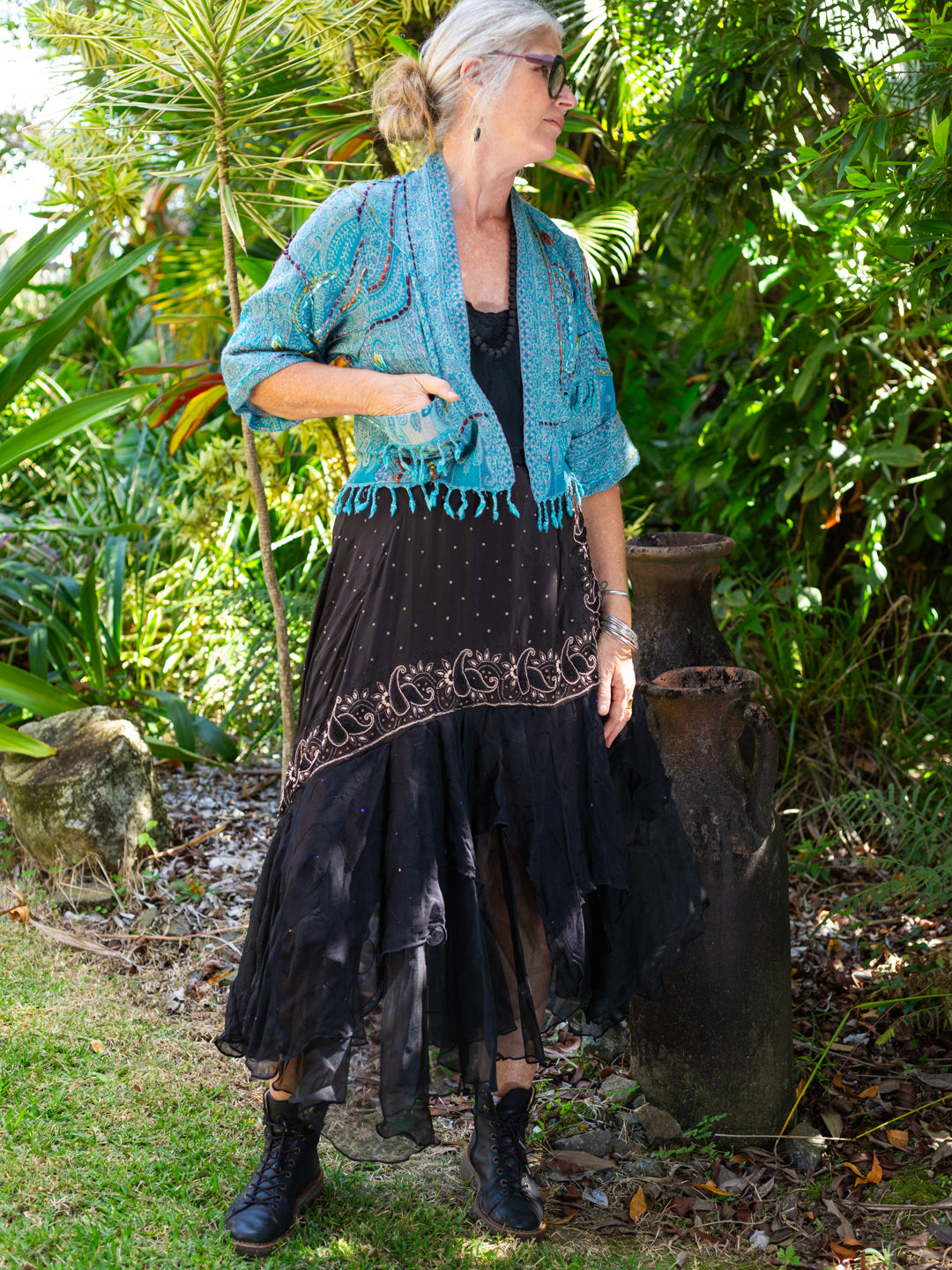 Woman in a black dress with floral patterns and a blue shawl standing in a garden.