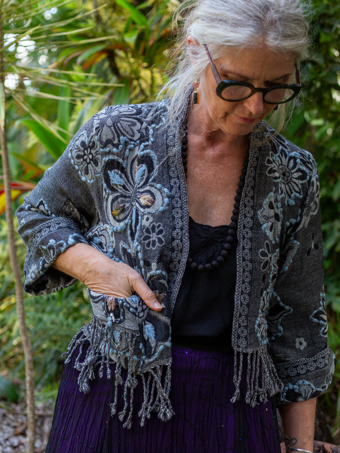 Woman wearing a patterned gray cardigan and purple skirt outdoors.