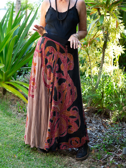 Person wearing a black top and a long, patterned skirt in a garden setting