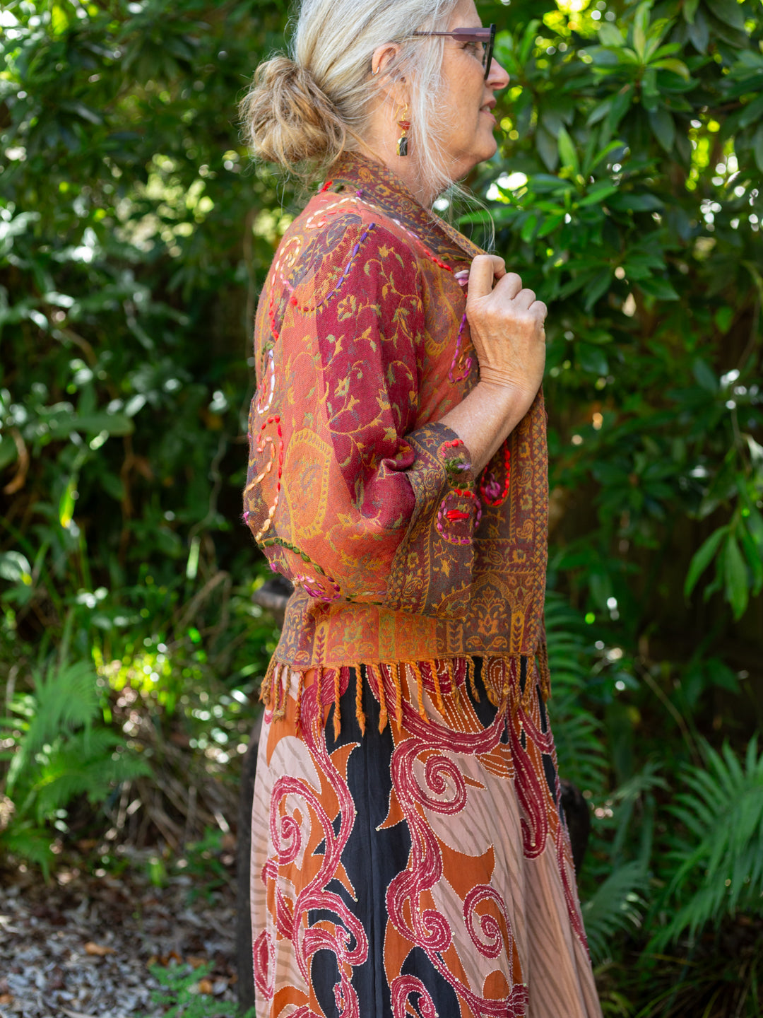 Woman wearing a patterned outfit with a fringed jacket in a garden setting