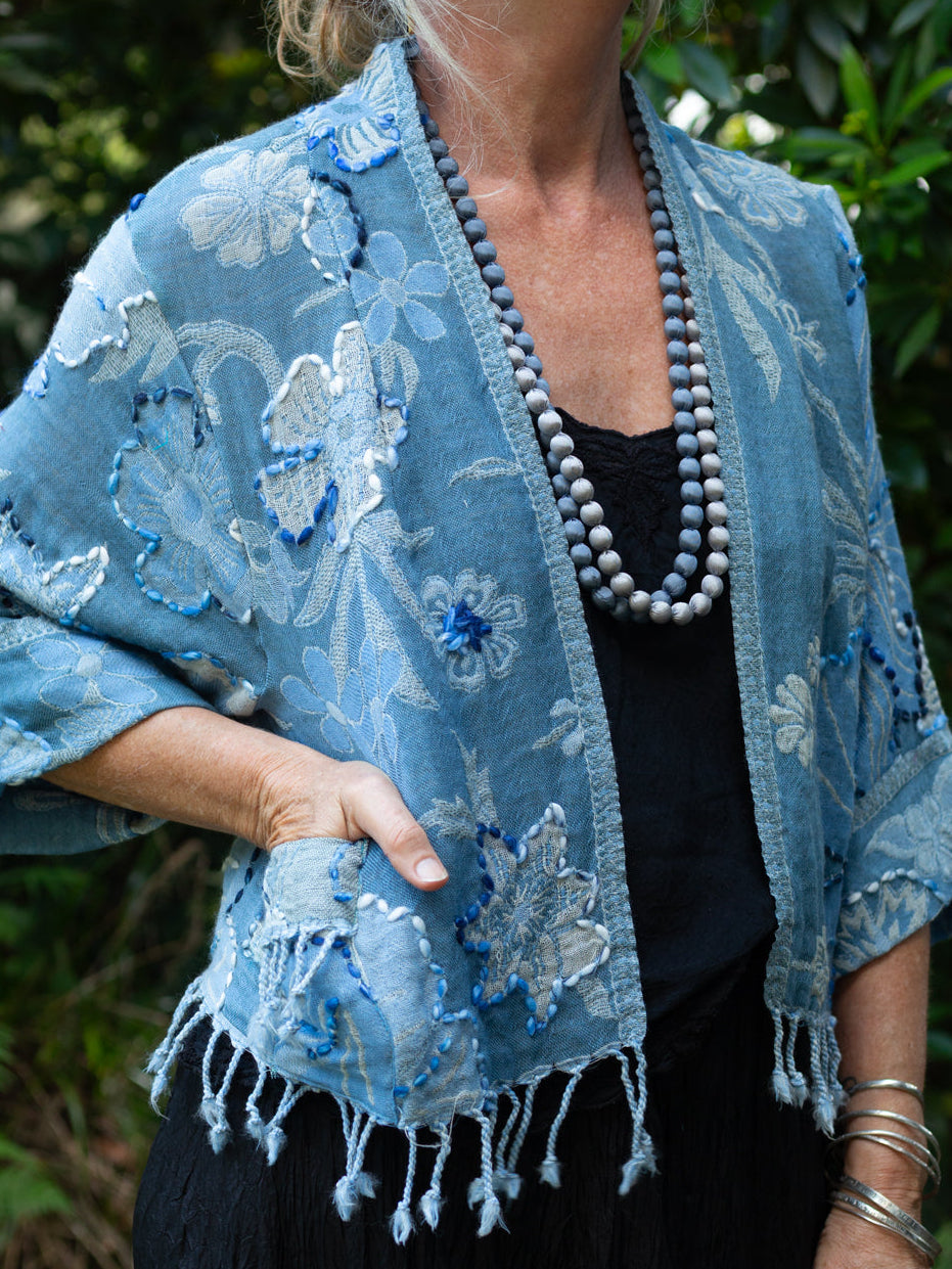 Woman wearing a blue embroidered shawl outdoors with greenery in the background