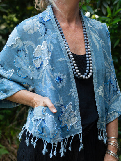 Woman wearing a blue embroidered shawl outdoors with greenery in the background