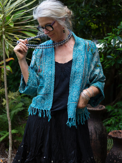 Woman wearing a blue textured cardigan outdoors with greenery in the background