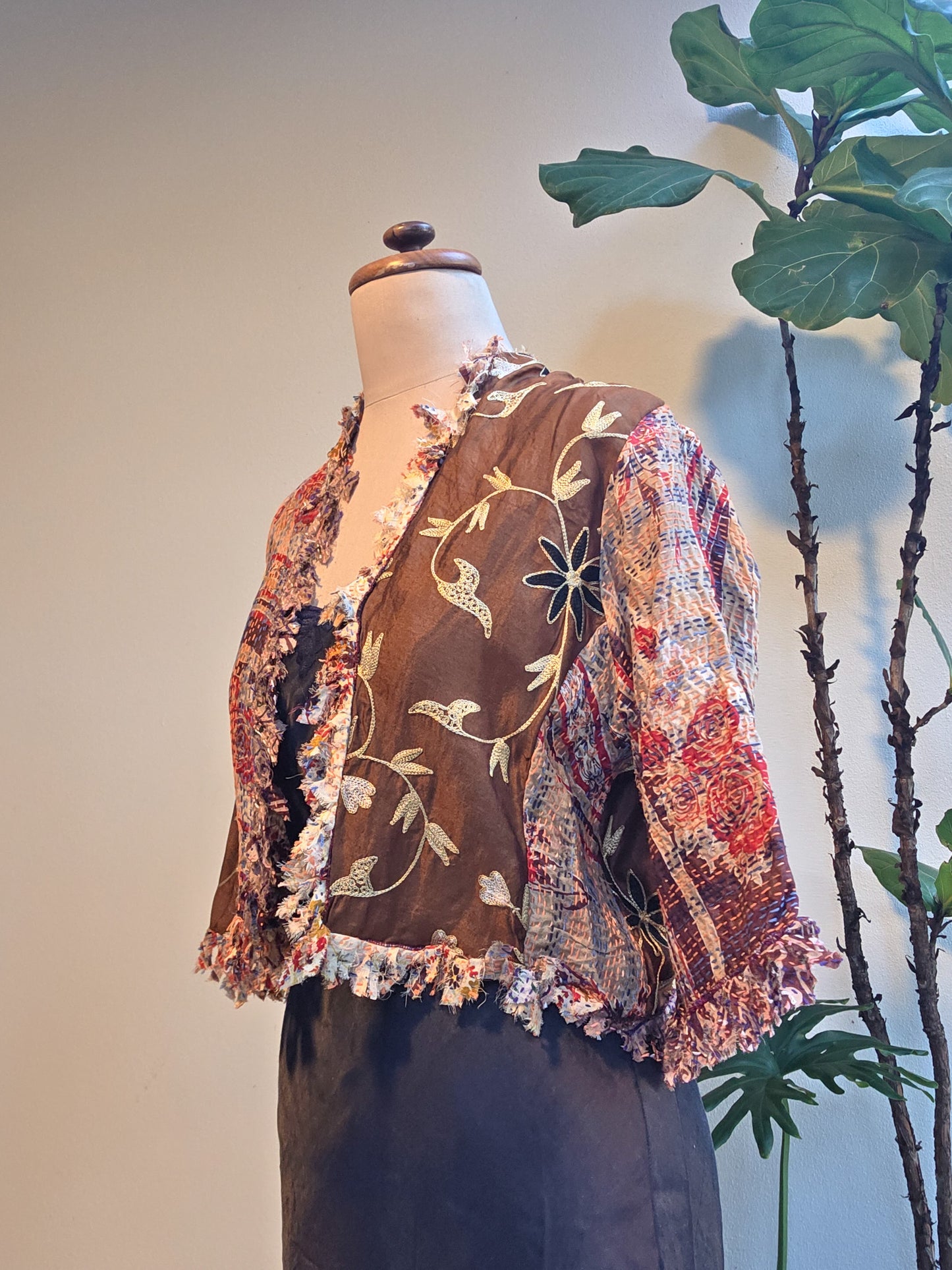Mannequin wearing a colorful embroidered jacket with a plant in the background, silver cocoonz