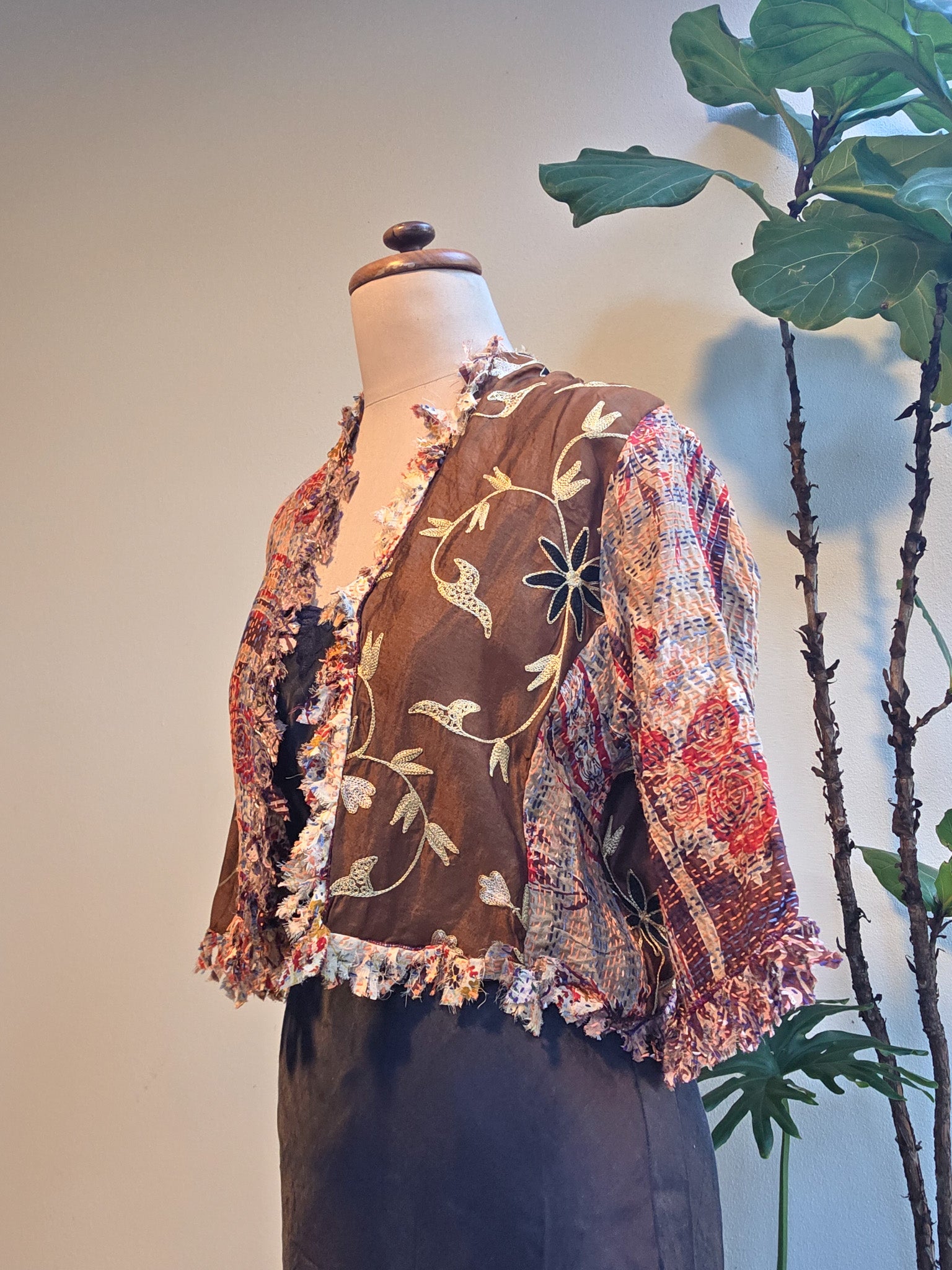 Mannequin wearing a colorful embroidered jacket with a plant in the background, silver cocoonz