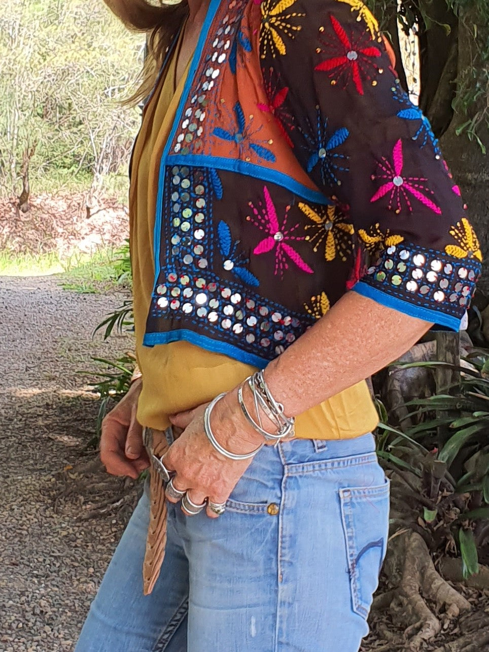 Side view of lady standing in a bohemian outfit of jeans, boots, belt and a sequinned jacket