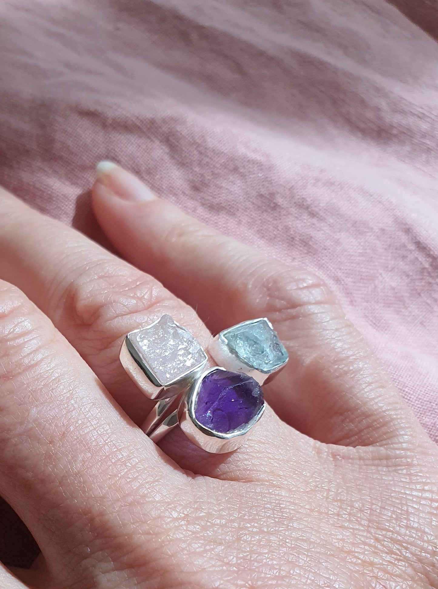 A silver ring with three raw cut crystals in blues and purples