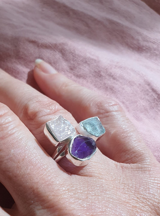A silver ring with three raw cut crystals in blues and purples