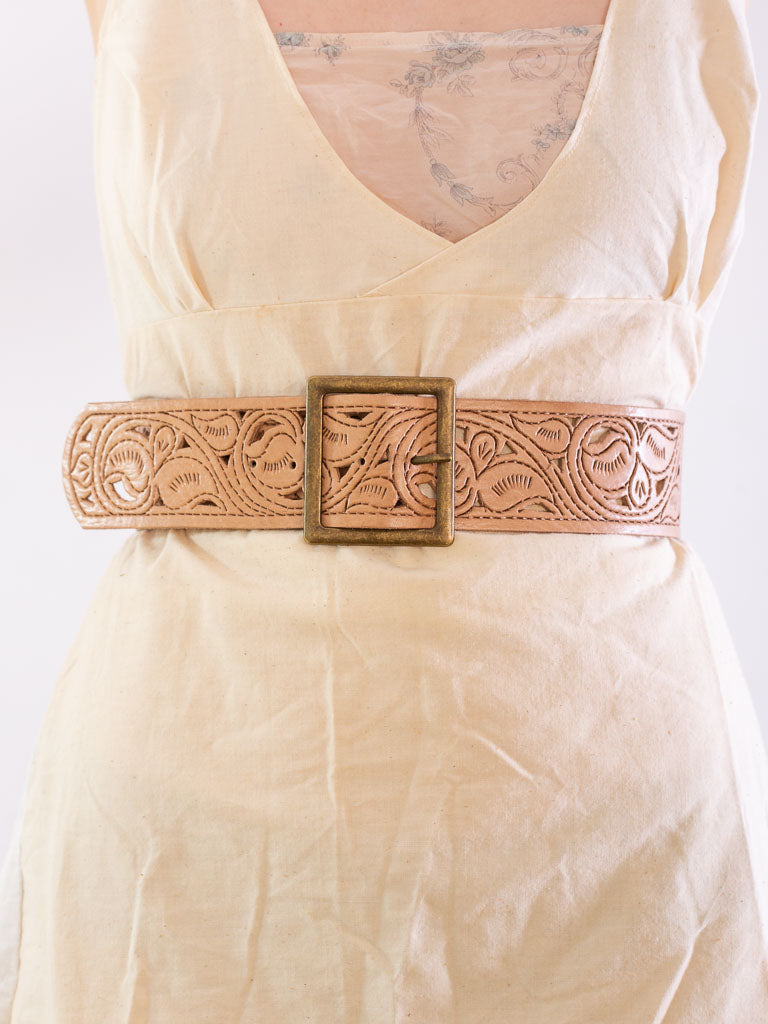 close up of models waist wearing a wide tan leather belt with a square brass buckle.The leather has a scroll design tooled into it