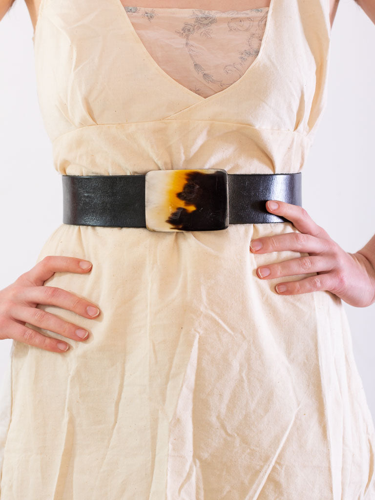 close up of models waist wearing a plain black leather belt with a rectangular bone buckle.